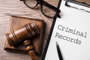 Flat lay of a clipboard displaying the words 'CRIMINAL RECORD' alongside a gavel on a wooden table, symbolizing legal proceedings and justice.