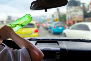 A man drinking alcohol while driving, putting himself and others at risk due to impaired judgment, delayed reaction time, and potential legal consequences.