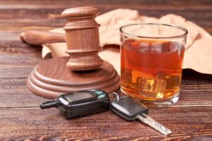 Car keys, a gavel, and a glass of whiskey on a wooden table, symbolizing the serious crime of drinking and driving with legal repercussions.