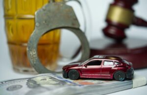 DUI concept: A car placed on a banknote beside a glass of beer and a gavel, symbolizing the financial and legal consequences of drinking and driving.