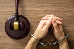 Handcuffed Convict, Law offender and Justice. Court sentence Prison. Handcuff locked and judge gavel on a wooden table, top view. 