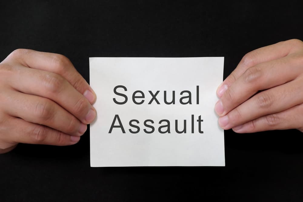 Sexual assault crime or rape mug shot concept. Criminal hands holding paper placard with written word in dark black background.