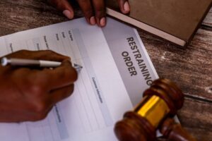 Hands filling out a restraining order form with a gavel nearby. Legal protection, domestic violence, court order concept.